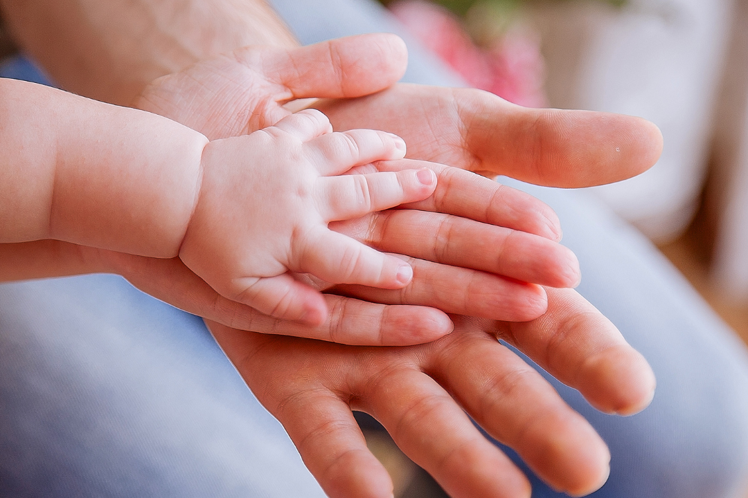 infant hand resting on 2 adult hands